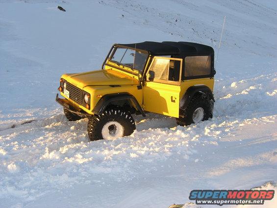 Yellow Land Rover Defender 90 in snow, 3/4 front view, soft top