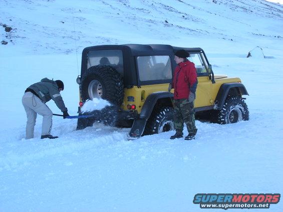 Yellow 2001 Jeep TJ stuck in deep snow, two people digging it out