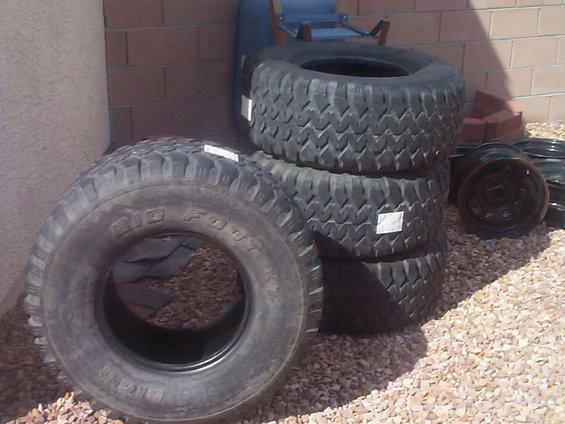 Stack of off-road tires, one labeled 'BIG FOOT'. Several black rims are visible to the right