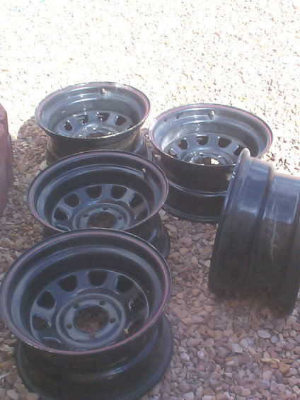 four black steel wheels stacked on gravel, one wheel on the right is on its side