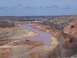 2004 Aston Martin Virage - A wide shot captures a muddy river winding through a desolate landscape with several vehicles parked along its banks.