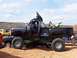 2004 Aston Martin Virage - A modified black truck with large tires and a dirt bike in the bed sits in sandy terrain with other vehicles nearby.