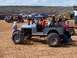2004 Aston Martin Virage - A heavily modified jeep with oversized tires and a roll cage sits on sandy ground, with other vehicles and spectators in the background.