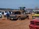 2004 Aston Martin Virage - Multiple vehicles are present at a muddy off-road event, with one truck deeply stuck in the sand.