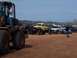 2004 Aston Martin Virage - A collection of modified trucks and vehicles are gathered on a dirt lot under a clear sky.