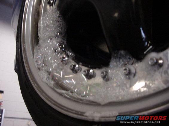 Close-up of a chrome wheel with lug nuts covered in soap bubbles