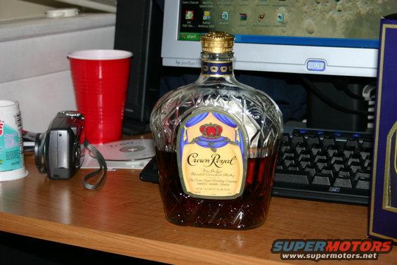 Crown Royal bottle with red cup, camera, and computer keyboard on desk