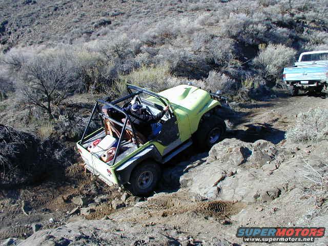 Yellow off-road vehicle with roll cage on rocky terrain, driver visible