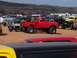 2004 Aston Martin Virage - Several modified trucks and off-road vehicles gathered on a sandy terrain under a cloudy sky.