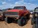 2004 Aston Martin Virage - A red lifted pickup truck with oversized tires and a racing banner sits in a muddy lot with other vehicles.