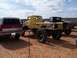 2004 Aston Martin Virage - A heavily modified yellow pickup truck with oversized tires sits on sandy ground next to a red SUV.