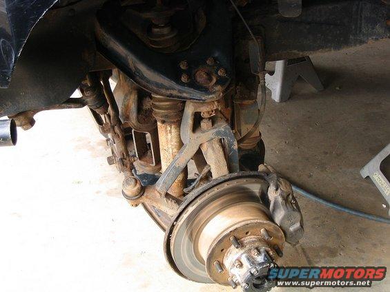 Close-up of a rusty front suspension and brake assembly with a rotor and caliper