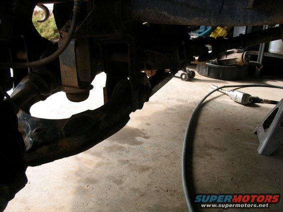Close-up of truck's front suspension parts, possibly during maintenance. Tools and jack stands visible