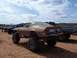 2004 Aston Martin Virage - A lifted 1970s muscle car with oversized tires sits on sandy terrain, with other trucks in the background.