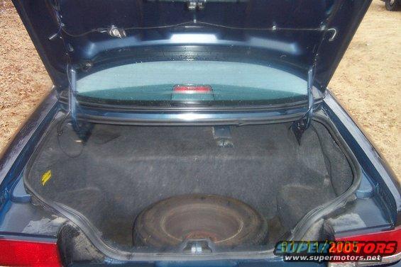 Car trunk open showing spare tire and carpeted interior. Watermark says SUPER 2005 TORS