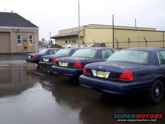 Four dark blue 2001 Ford Crown Victoria police cars parked in a wet lot