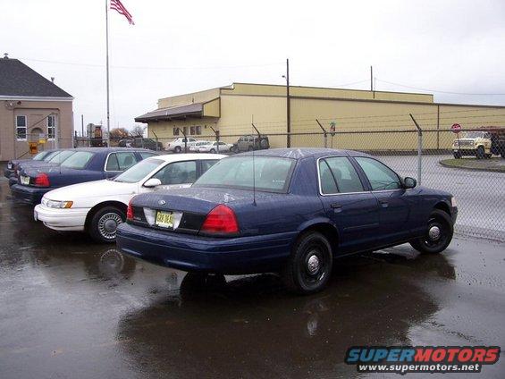 Dark blue 2001 Ford Crown Victoria police car parked in lot with other vehicles, license plate reads GR8 DEAL
