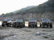 1988 Ford Bronco - Four SUVs, including a 1987 Ford Bronco, are parked in a line on a rocky shore with hills in the background.