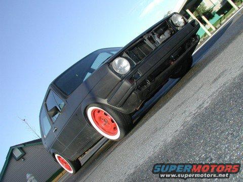 Black Volkswagen Golf GTI, Mk2, with red steel wheels and white wall tires. Front grille removed