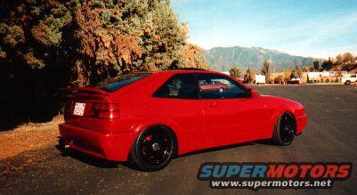 Red coupe with black wheels parked outside, mountains in background