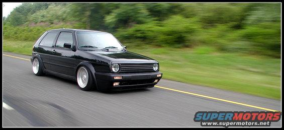 Black Volkswagen Golf GTI driving on a highway, lowered suspension, aftermarket wheels, motion blur