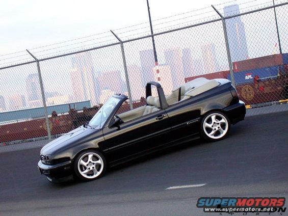 Black convertible with tan interior parked on a street with a city skyline in the background