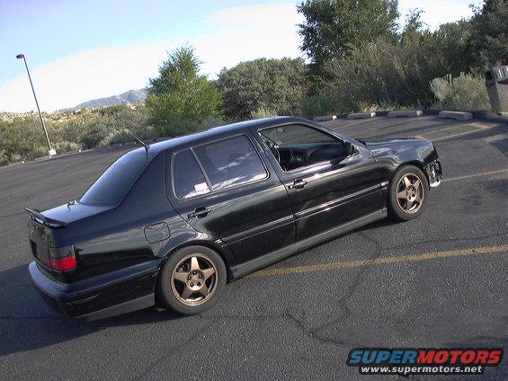 Black sedan with aftermarket wheels, front bumper removed, seen from 3/4 front angle