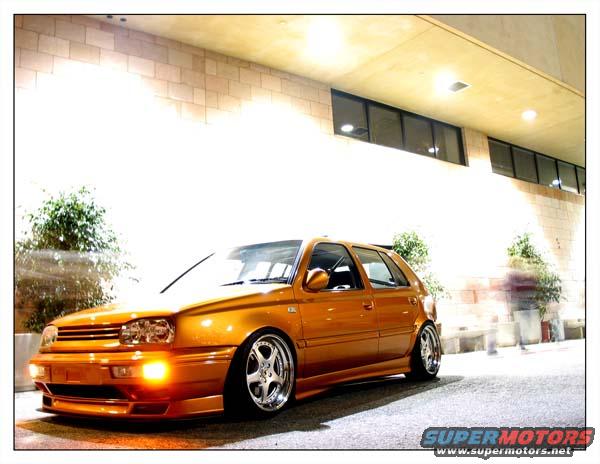Orange hatchback with custom wheels parked outside a building