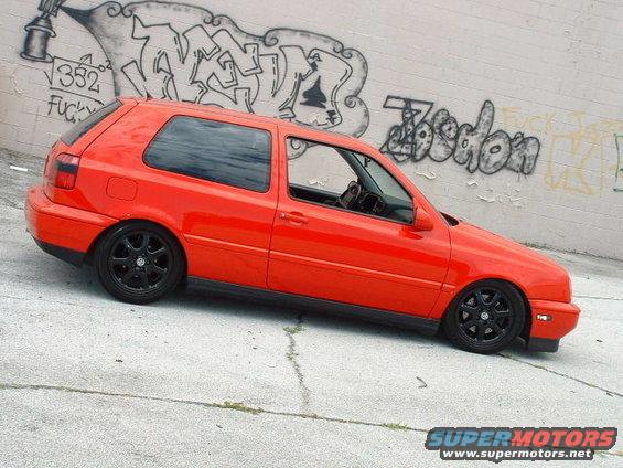 Red hatchback with black wheels parked against a graffiti-covered wall