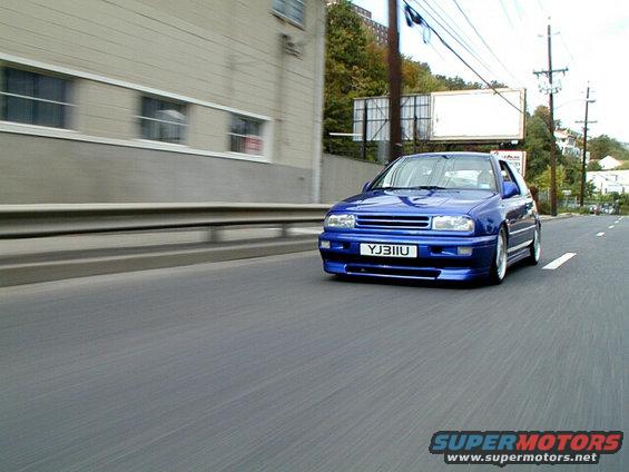 Blue hatchback with custom body kit driving on a road
