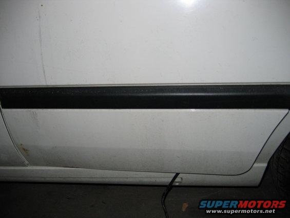 Close-up of white car door with black trim and rust spot