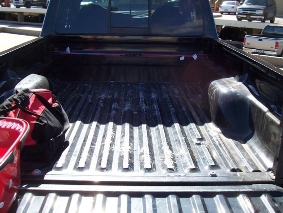 Truck bed with a red bucket and a duffel bag inside. Other vehicles are visible in the background