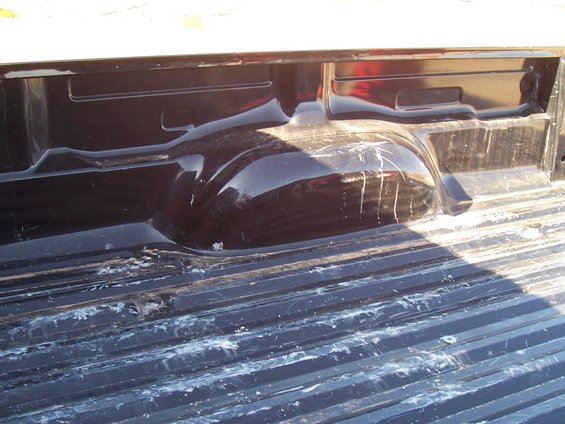 Black truck bed interior with visible scratches on the wheel well and white residue on the ribbed floor