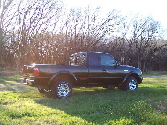 Black Ford Ranger pickup truck with an "EDGE" badge on the side, parked in a grassy field with trees in the background