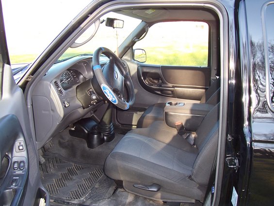 Interior of a black 2003 Ford Ranger showing dashboard, seats, and steering wheel with Ford logo