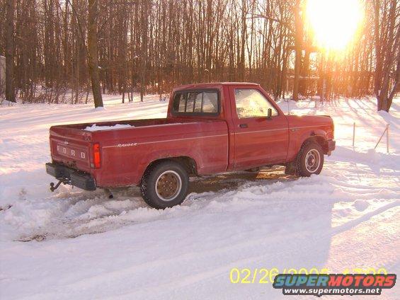 Red Ford Ranger pickup truck parked in snow, sun low in the sky