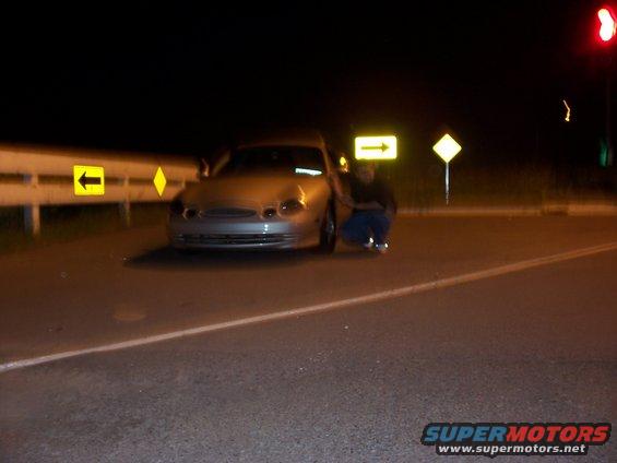 1998 Mercury Sable parked on road at night, person crouching beside it