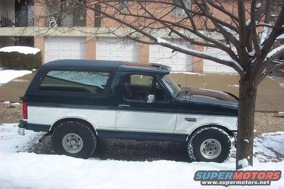 Dark green and white two-door Ford Bronco parked in snow, side view