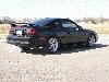 Black coupe with spoiler, rear 3/4 view. Likely a 1994-1998 Ford Mustang