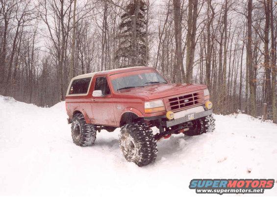 Red 1995 Ford Bronco with large off-road tires driving in snow, front 3/4 view