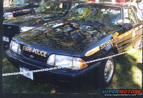 1991 Ford Mustang SSP police car with 'STATE POLICE' on hood and 'STATE TROOPER' on fender. Another police car is behind it