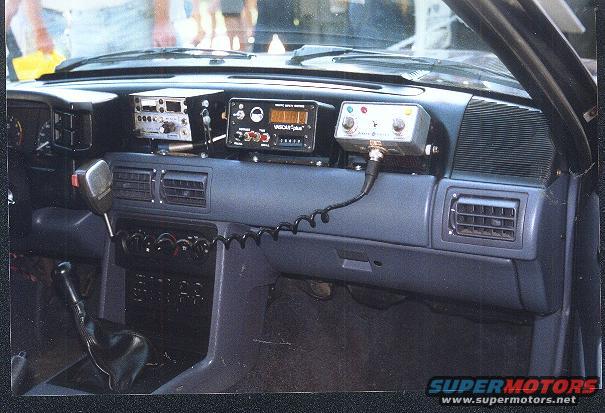 Car interior showing dashboard with multiple radio units and a microphone. Looks like a 1991 Ford Mustang