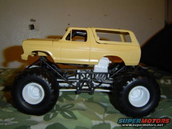 Yellow 1979 Ford Bronco model with oversized tires and exposed engine, viewed from the side