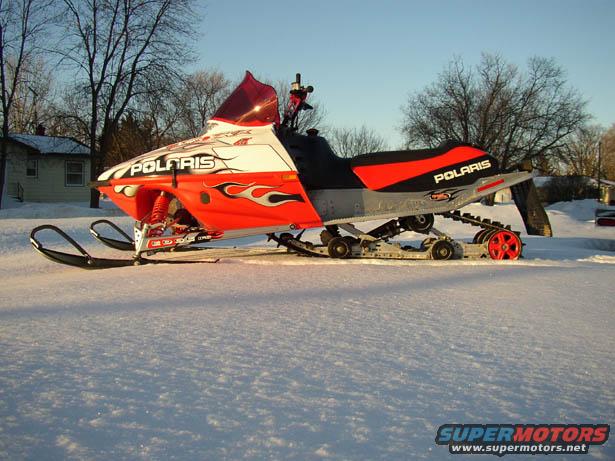 Orange and white Polaris snowmobile with flame decals, side view, parked in snow