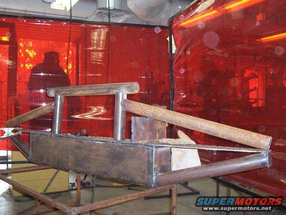 Custom metal bumper assembly on a welding stand, with red welding curtains in the background