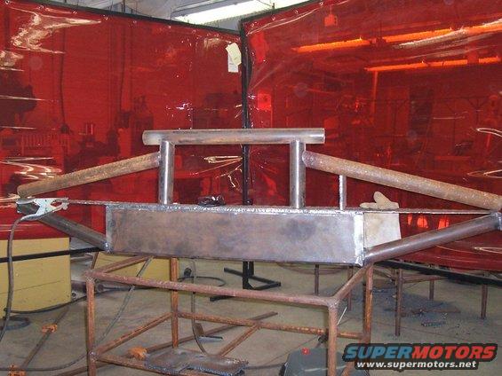 Custom metal bumper being fabricated in a workshop with red welding curtains in the background