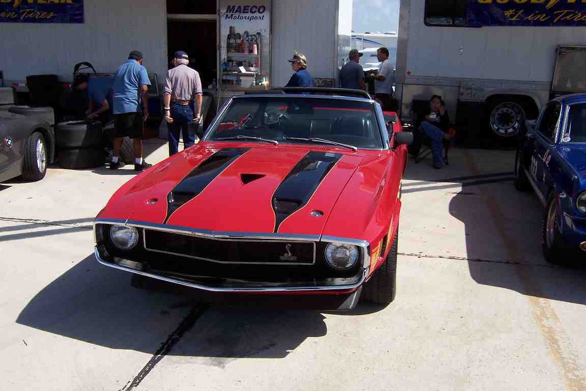 Red convertible muscle car with black stripes on hood, parked next to a blue car