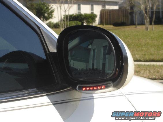 White car side mirror with integrated LED turn signal and reflection of a house