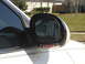 1997 Lincoln Mark VIII - Side mirror assembly on a white vehicle shows a turn signal and a reflection of a residential building.