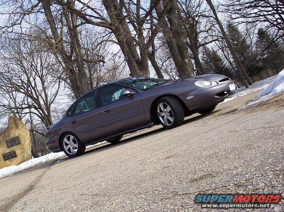 Gray Ford Taurus parked on a road with trees and snow in the background